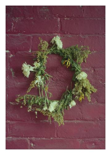 A collaged oil painting, the images are oriented in varying directions. It depicts a set of hands clasping red spotted flowers, a single lit white candle, a woman looking out onto a highway through veiled transparent curatins and a young girl at the table while her mother works in the kitcen behind her.
